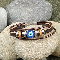 Evil Eye Bracelet on a bed of river rocks, highlighting the rich contrast between the smooth beads and rustic leather.