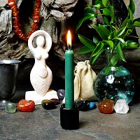 A lit forest green chime candle, in a personal altar display, showing how it might be used in a ritual or ceremonial setting.