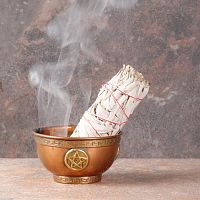 Smoldering White Sage Herb Bundle with a trickle of smoke, propped in a small copper bowl that sits on fireproof tile surface