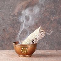 Smoldering Sage and Eucalyptus Bundle with a trickle of smoke, propped in a small copper bowl that sits on fireproof surface.
