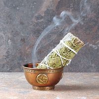 Smoldering Sage and Pine Bundle with a trickle of smoke, propped in a small copper bowl that sits on fireproof tile surface.