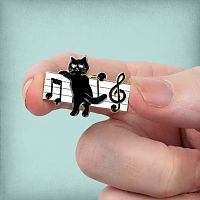 The Music Cat Enamel Pin held in someone's fingertips, showing its small size, and its black, white, and gold colors.