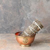Smoldering Mugwort Herb Bundle with a trickle of smoke, propped in a small copper bowl that sits on fireproof tile surface.