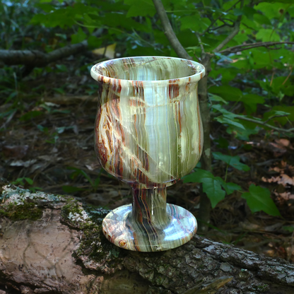 Green Onyx Goblet showing natural bands of earthy greens and browns, displayed on a mossy tree trunk in a forest setting.